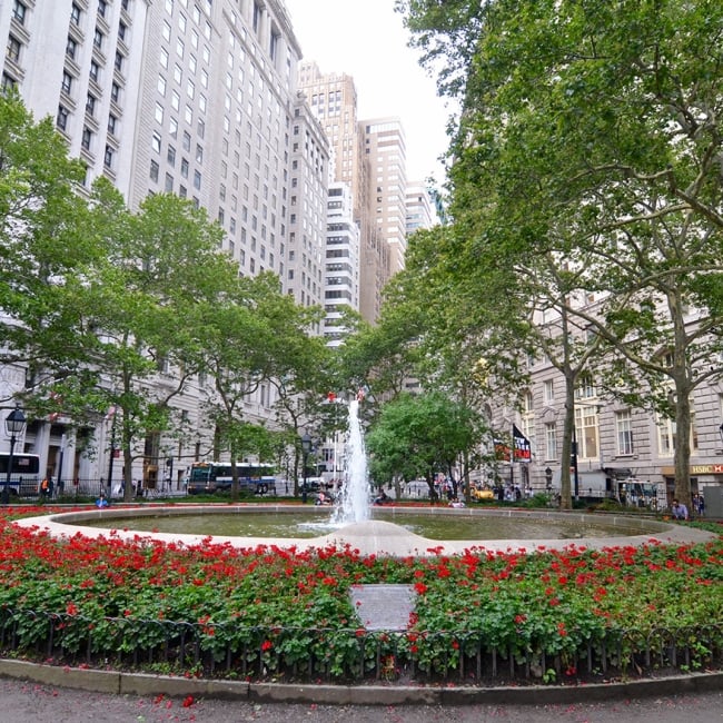 large fountain surrounded by large buildings and lush greenery