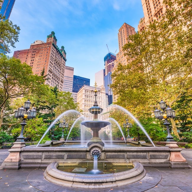 large fountain surrounded by tall buildings and trees