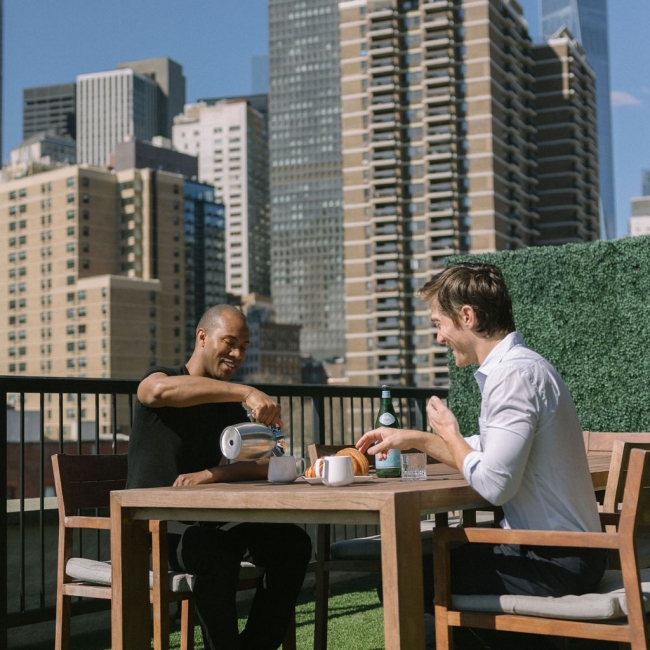 two men drinking coffee on a private terrace with the manhattan skyline in the background