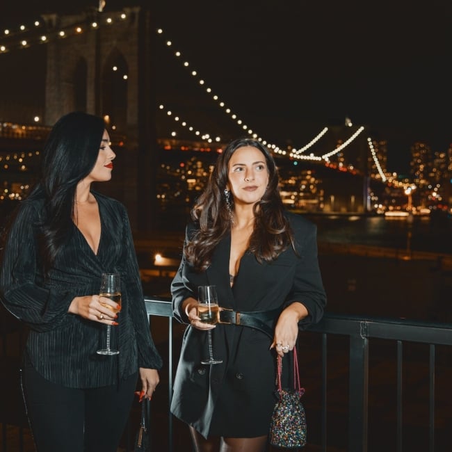 Two women in front of brooklyn bridge at night