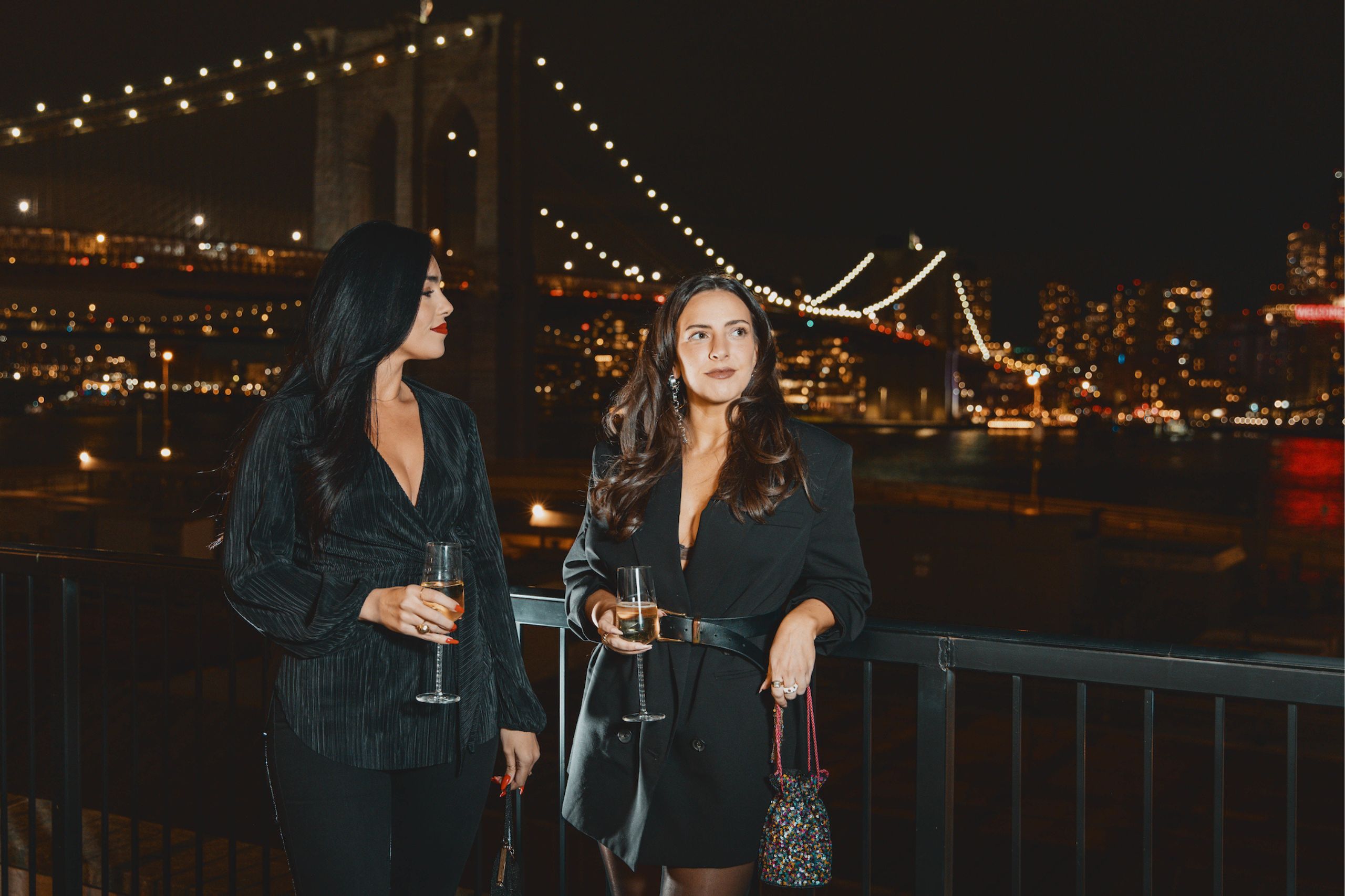Two women in front of brooklyn bridge at night